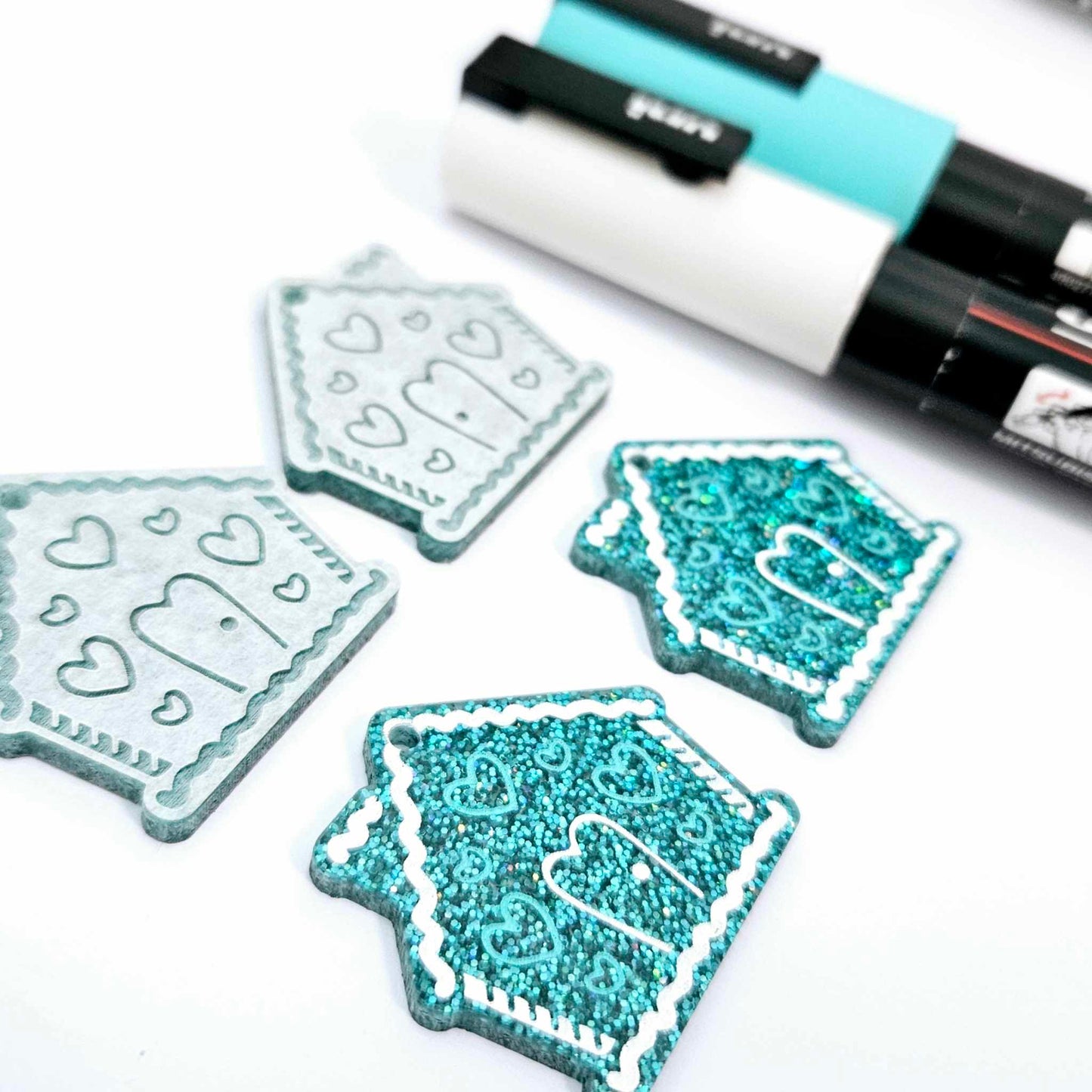 teal glitter acrylic gingerbread house earring blanks that have been paint filled with aqua green and white posca paint pens
