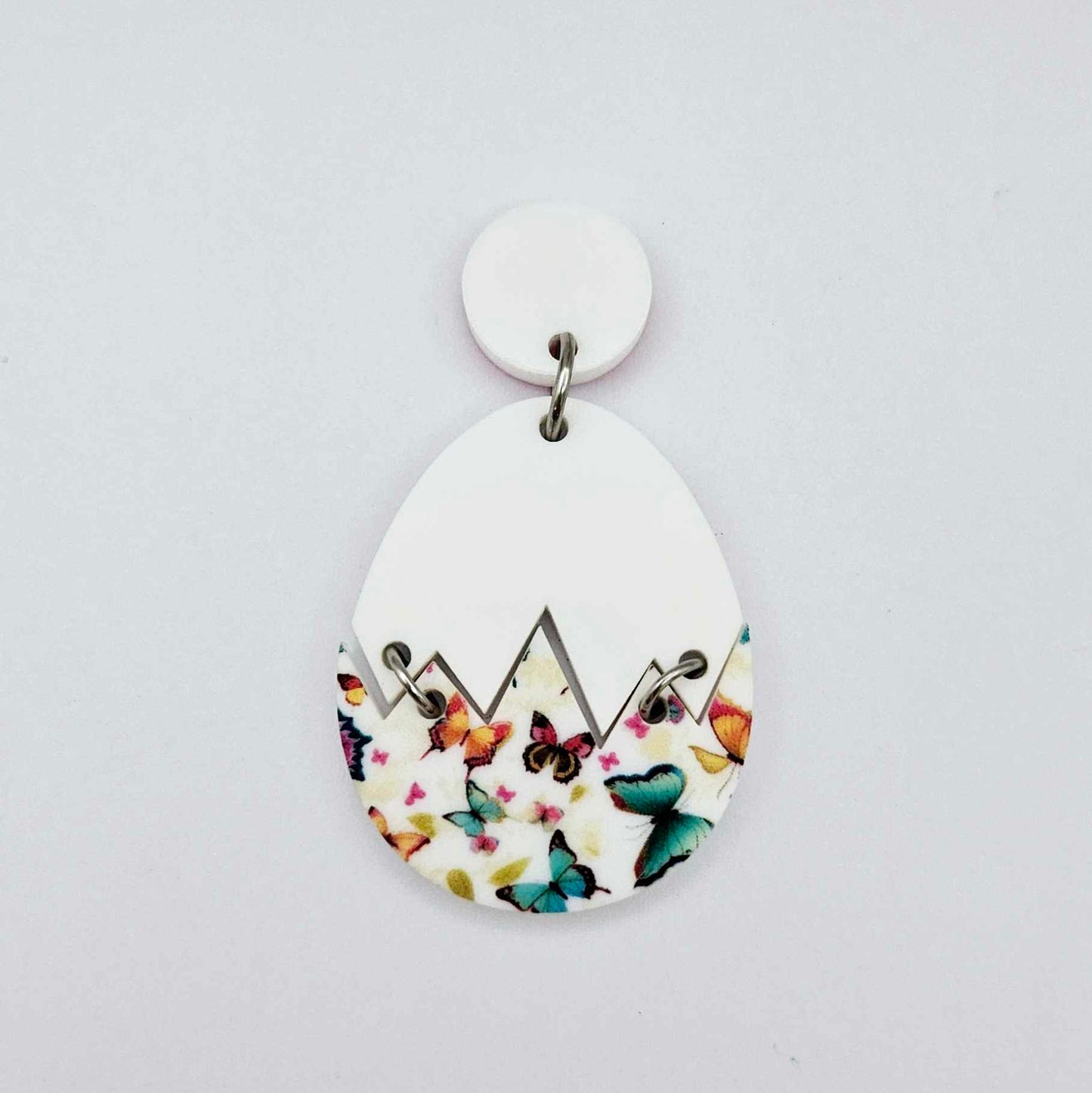 Assembled cracked egg acrylic dangle earring blank with white top and butterfly UV printed bottom, hanging from a 14mm white earring topper