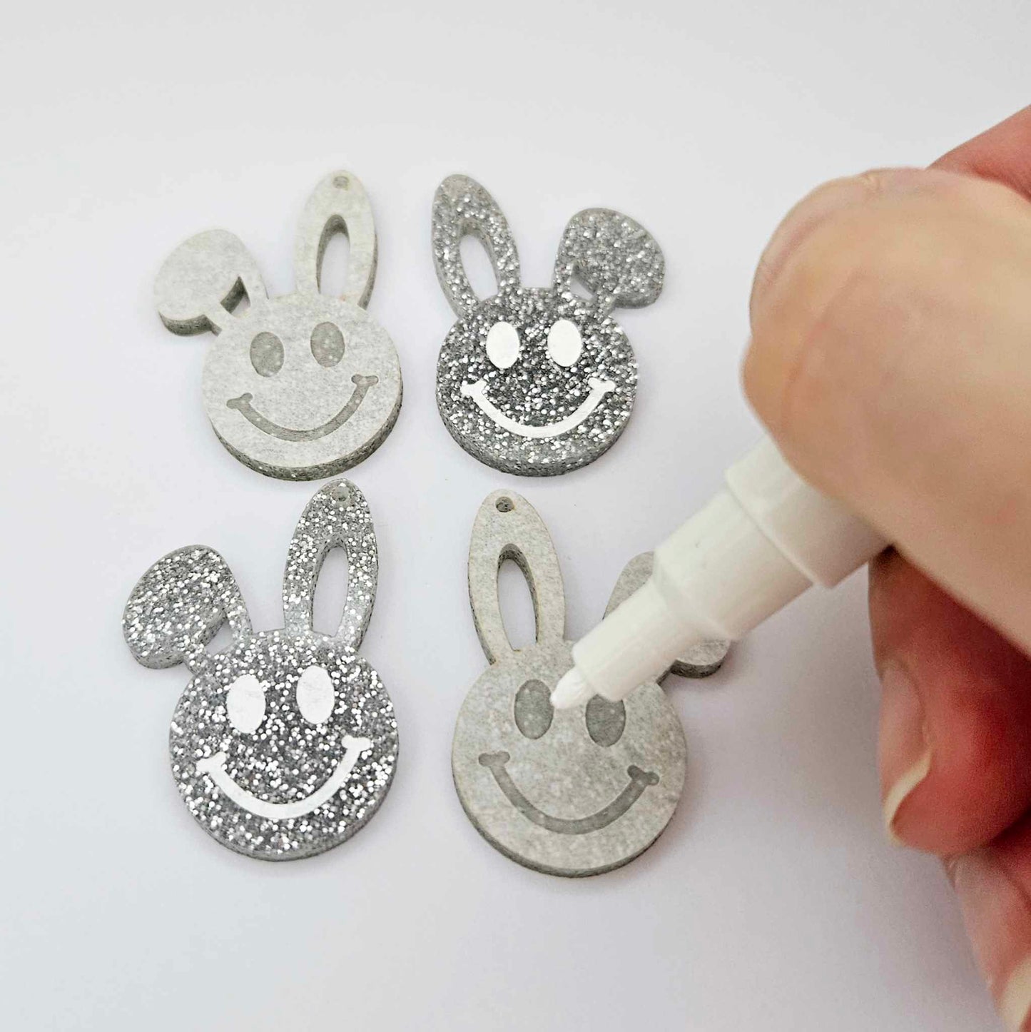 38mm silver glitter acrylic bunny dangle blanks with engraved smiley face, two paint filled white and two others unfilled with protective film on, shown with a White Posca paint pen