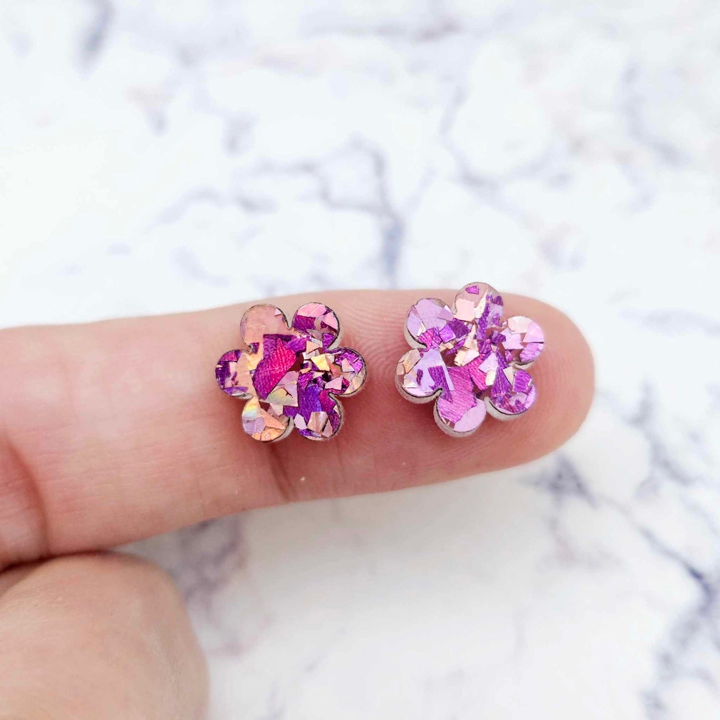 Two 10mm glitter flower stud blanks in Chunky Unicorn colour, shown on a finger for size reference