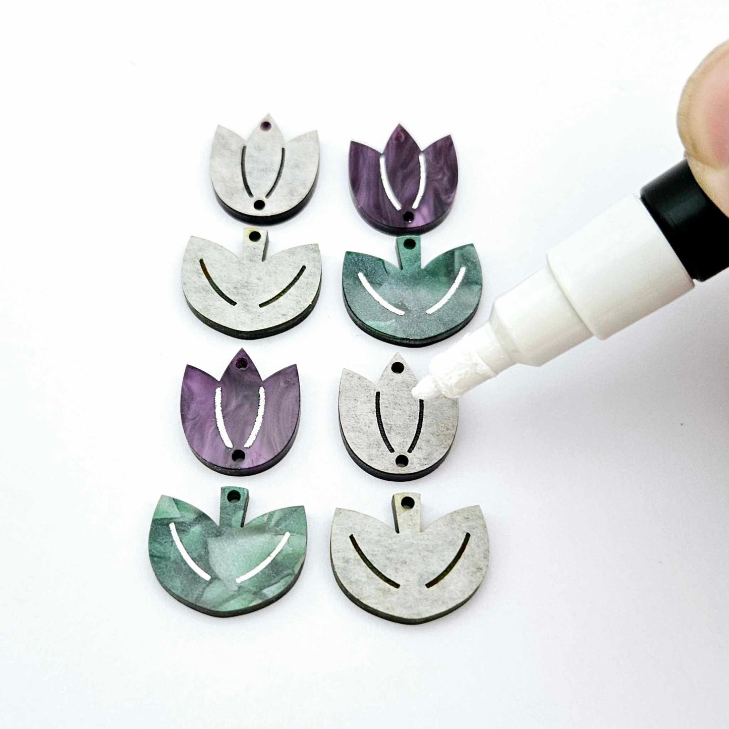 Two-piece tulip acrylic dangle blanks in purple marble and green mineral acrylic, paint filled white on one pair with remaining pair unfilled, shown with a white Posca paint pen