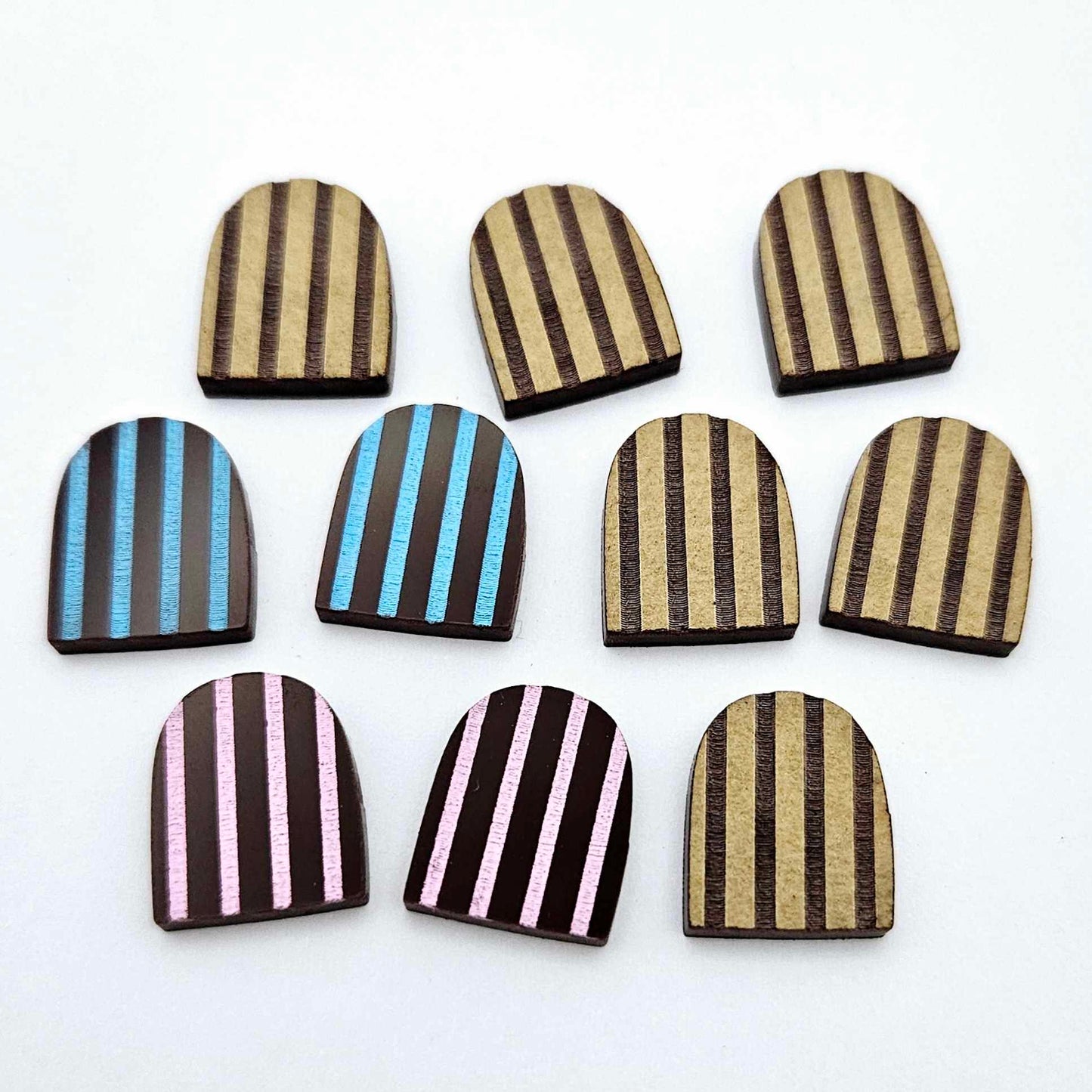 Chocolate brown striped arch stud blanks with engraved stripes, one pair paint filled light pink, one pair painted filled light blue, with additional unpainted pieces shown with protective film on