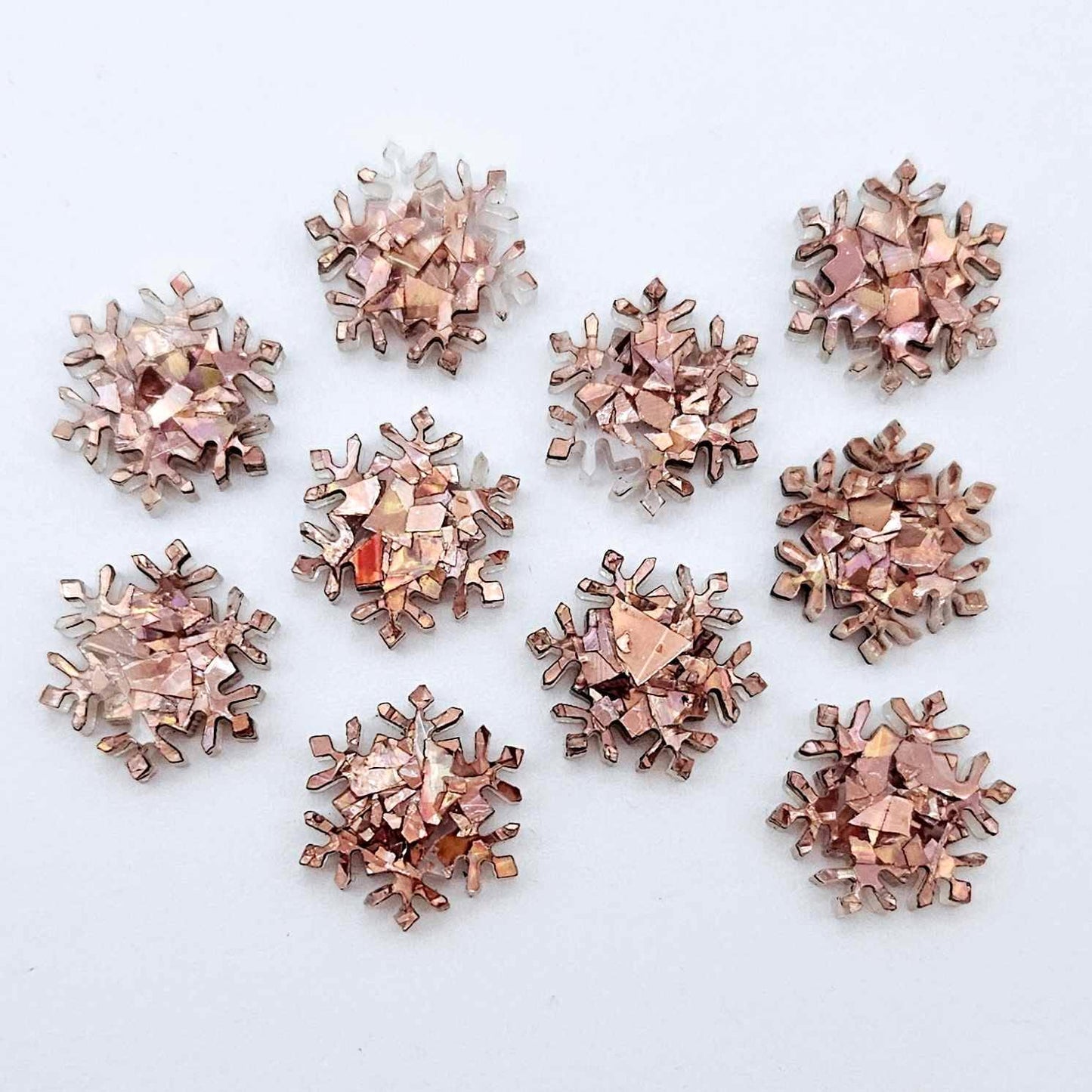 Five pairs of 16mm chunky rose gold glitter acrylic snowflake stud earring blanks laying flat.
