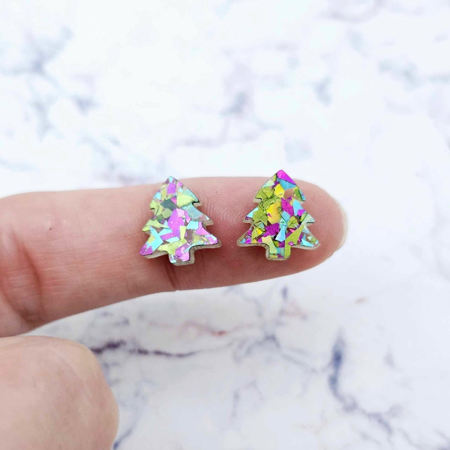 One pair of 12mm chunky peacock glitter acrylic Christmas tree stud earring blanks shown on a finger for size reference.