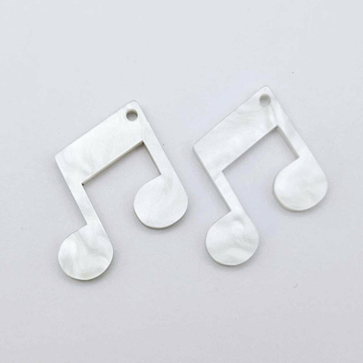 One pair of 35mm white marble acrylic music note earring dangle blanks laid flat together.
