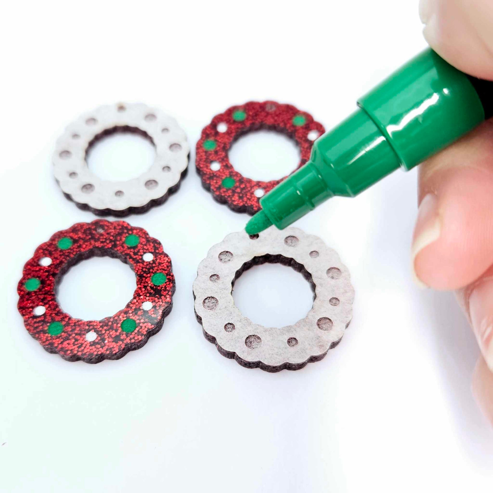red glitter acrylic wreath earring blanks that are being paint filled with green and white posca paint pens