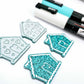teal glitter acrylic gingerbread house earring blanks that have been paint filled with aqua green and white posca paint pens