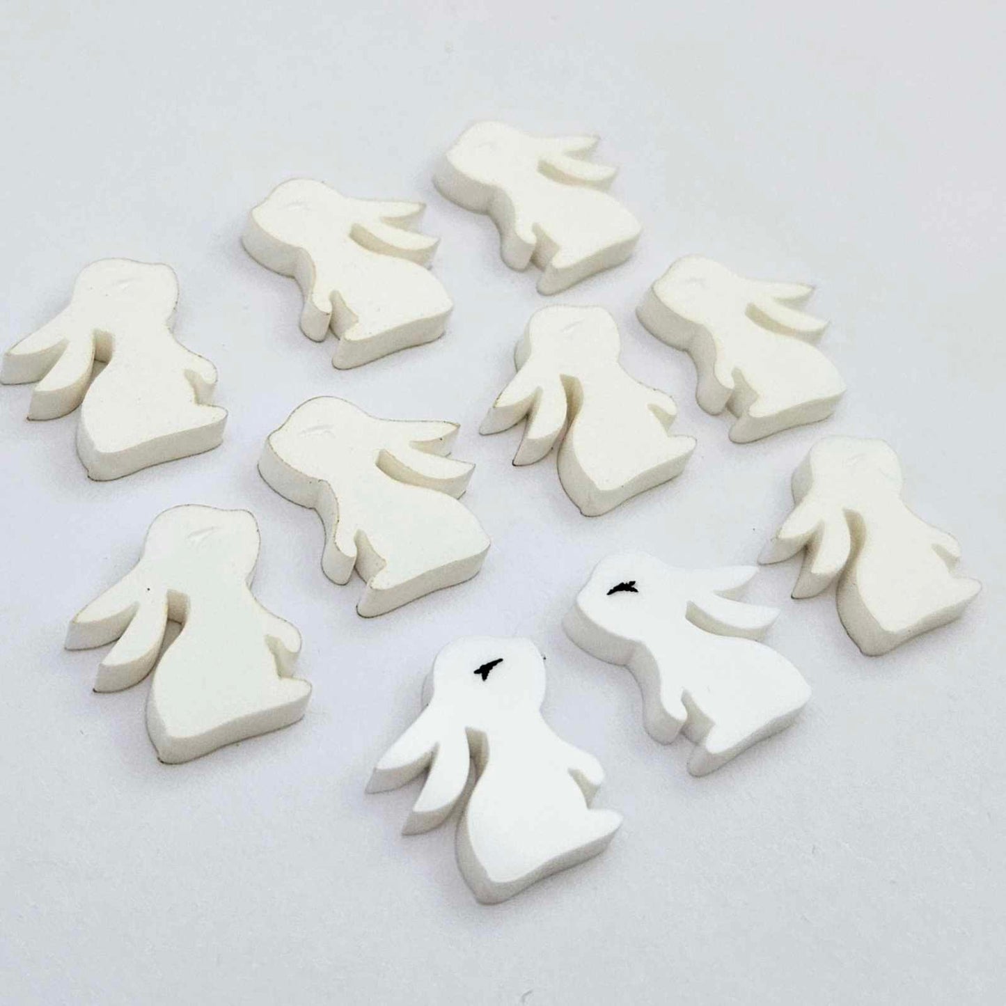 white acrylic bunny stud blanks showing finished paint filled black eyelashes on two studs, with the rest shown as supplied with protective film