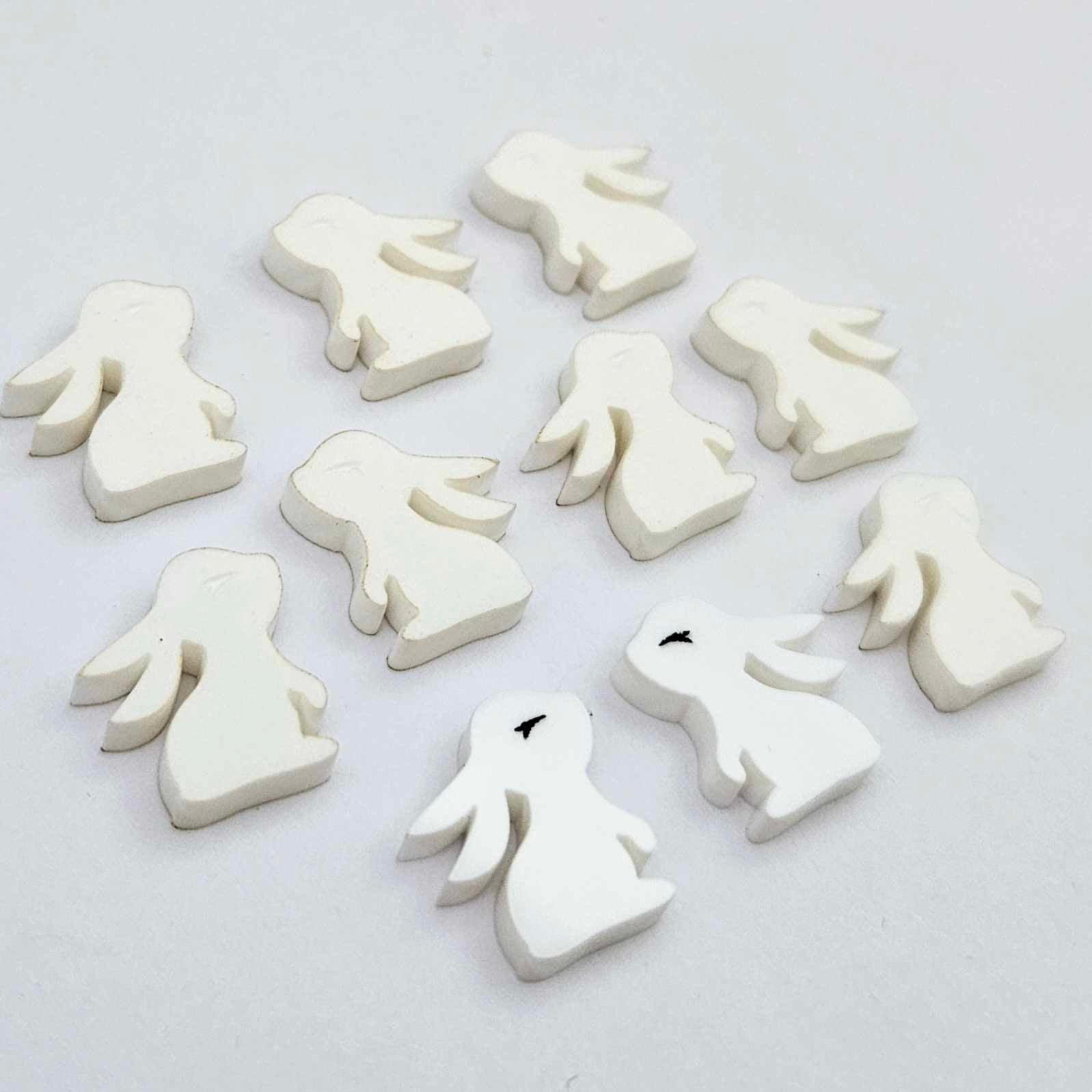 white acrylic bunny stud blanks showing finished paint filled black eyelashes on two studs, with the rest shown as supplied with protective film