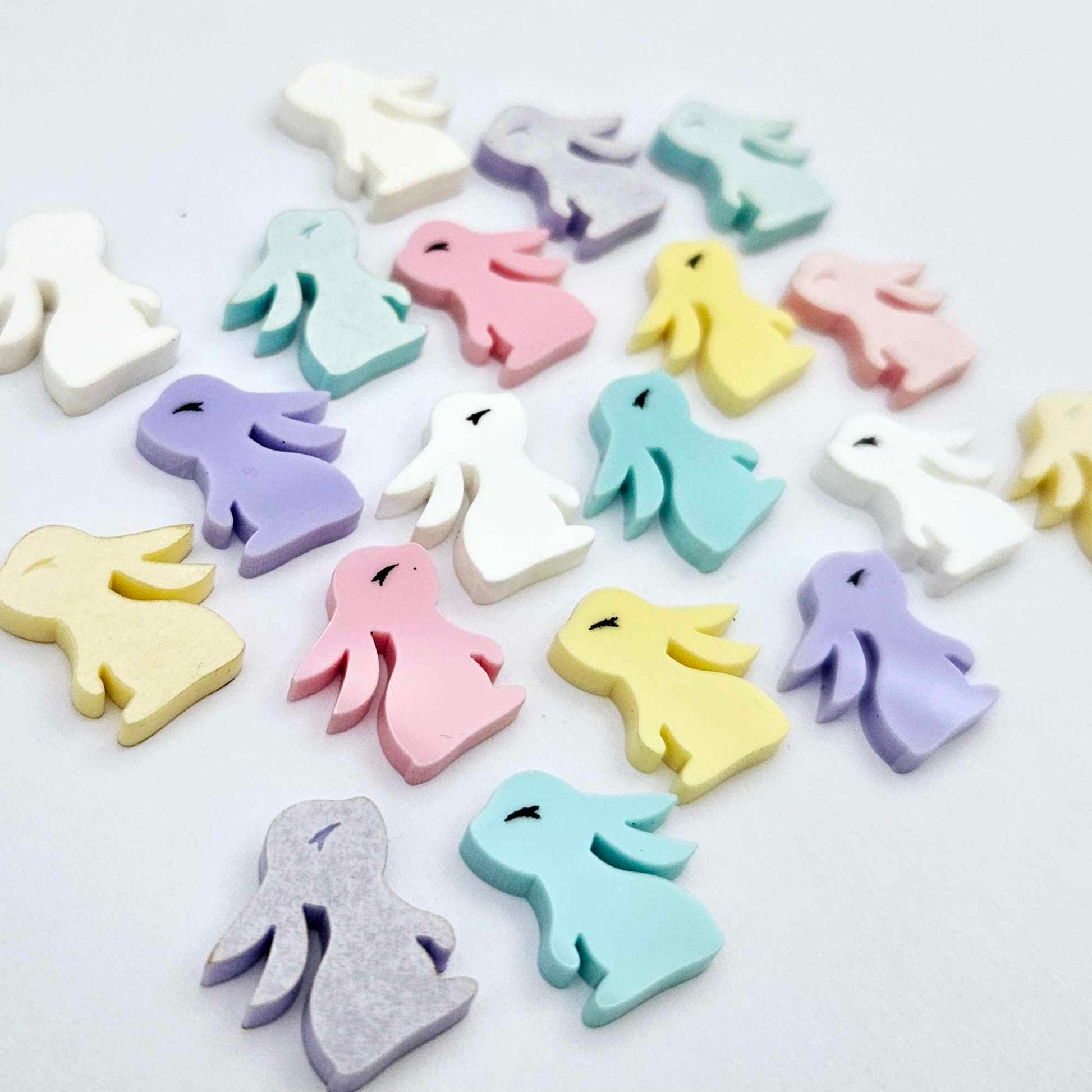Pastel yellow, pink, purple, aqua and white bunny stud blanks (mixed pack) showing finished paint filled black eyelashes on two studs, with the rest shown as supplied with protective film