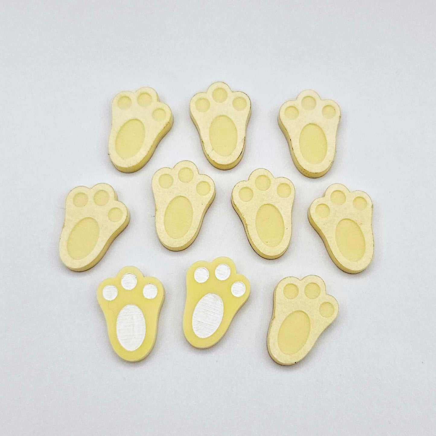 Pastel yellow bunny paw print stud blanks showing two paint filled white and several unpainted pieces