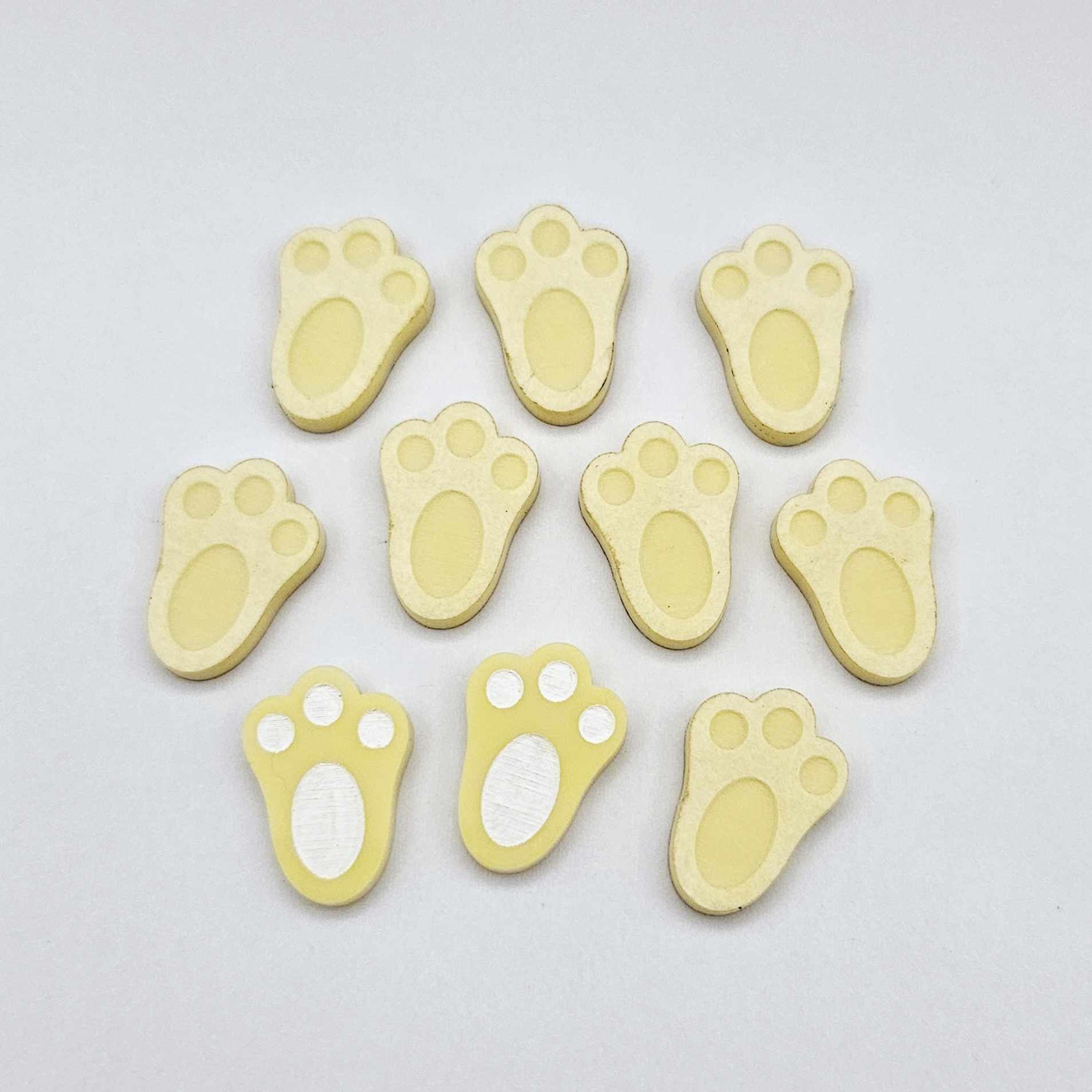 Pastel yellow bunny paw print stud blanks showing two paint filled white and several unpainted pieces