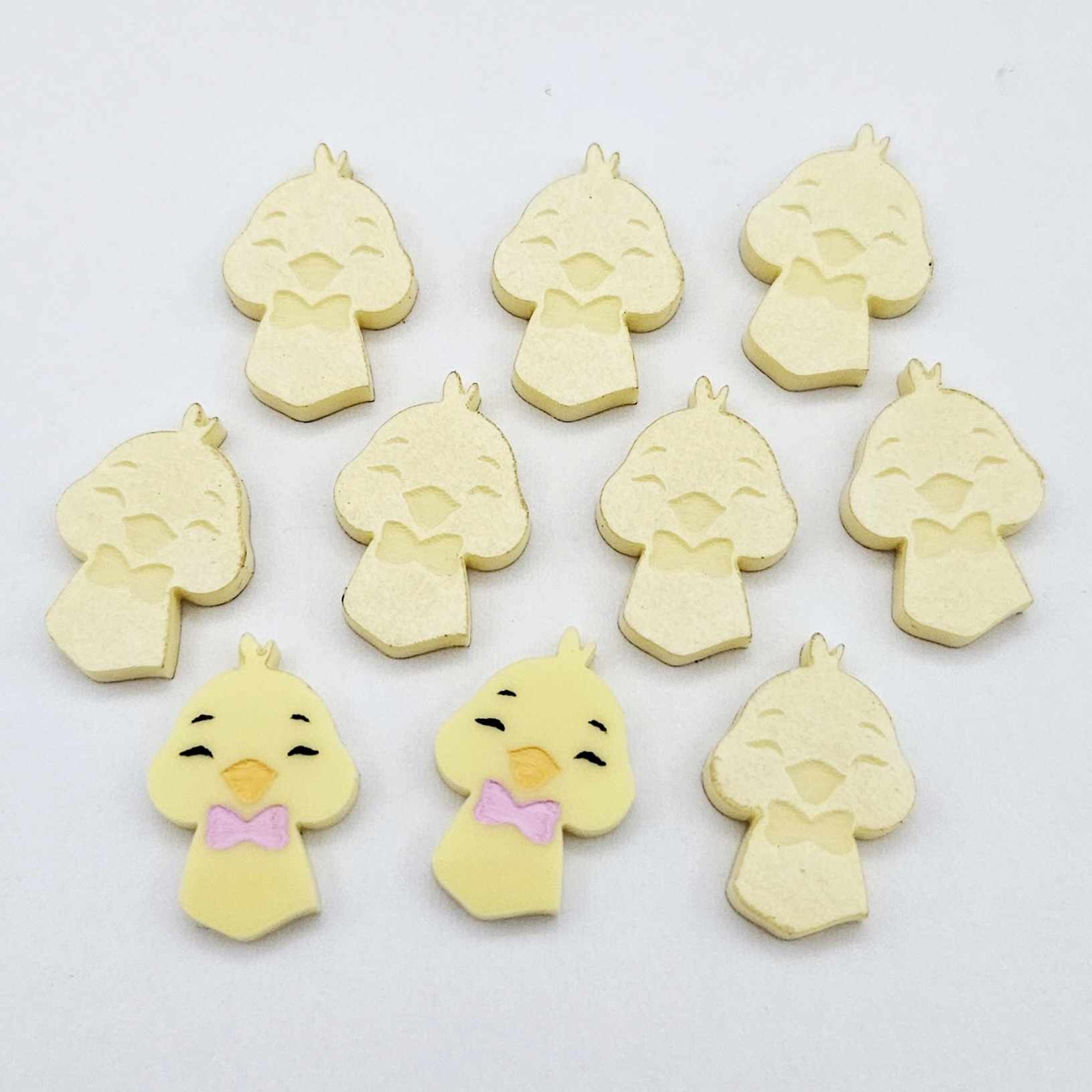 Pastel yellow acrylic chicken head stud blanks showing two paint filled examples and several unpainted 