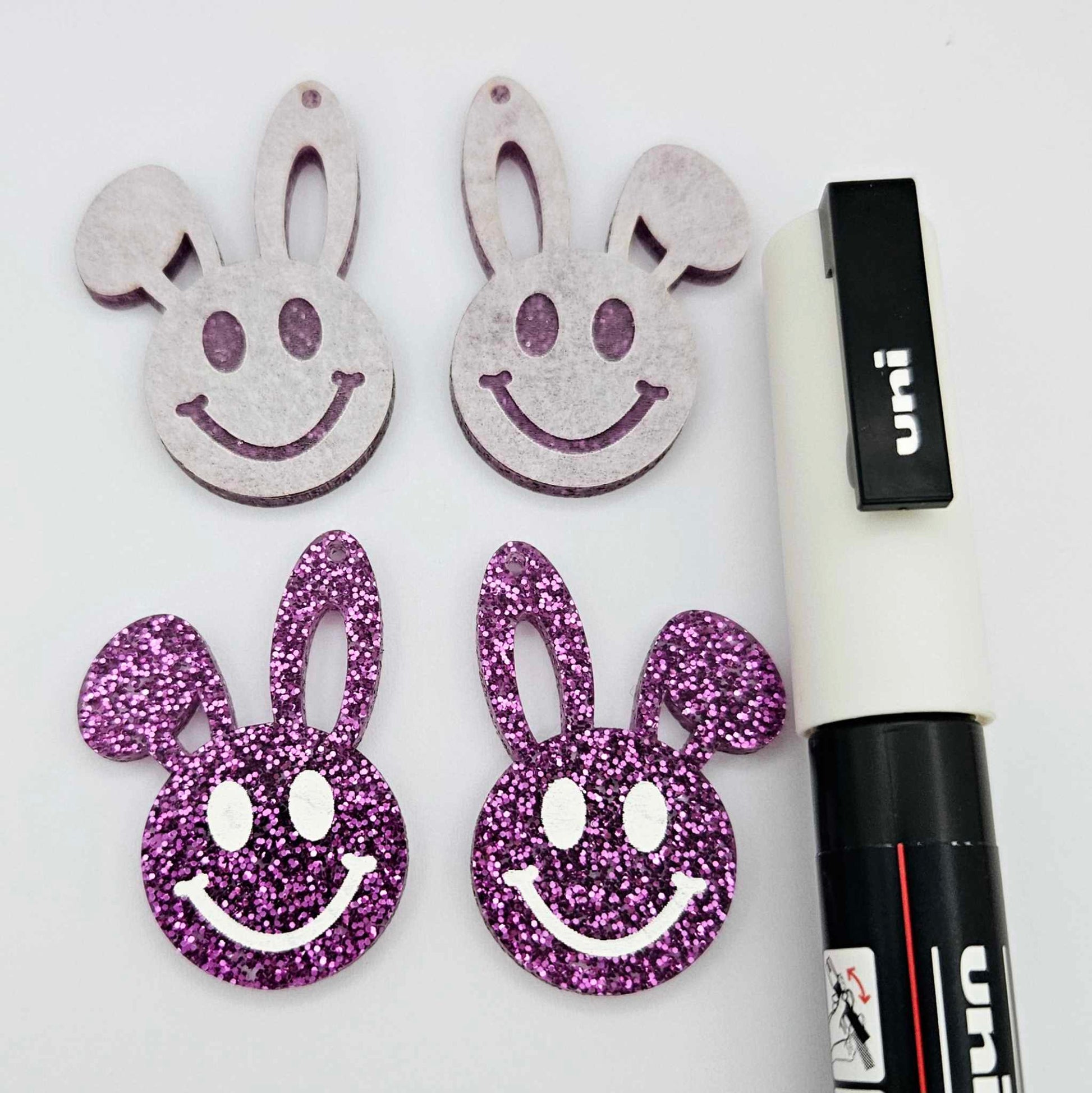 38mm purple glitter acrylic bunny dangle blanks with engraved smiley face, two paint filled white and two others unfilled with protective film on, shown with a White Posca paint pen