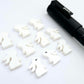 white acrylic bunny stud blanks showing finished paint filled black eyelashes on two studs, with the rest shown as supplied with protective film