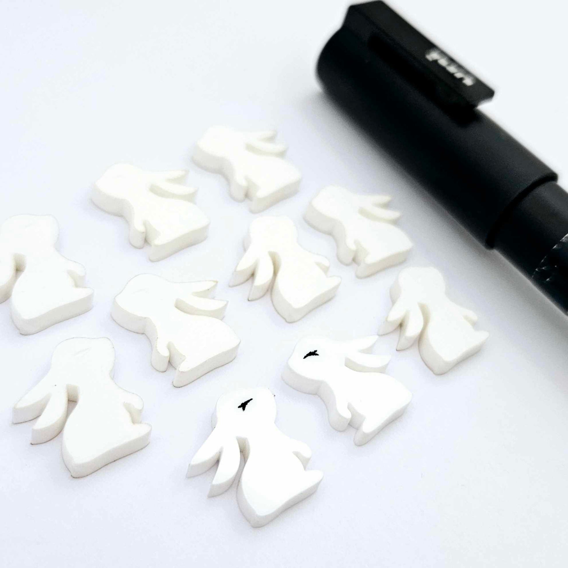 white acrylic bunny stud blanks showing finished paint filled black eyelashes on two studs, with the rest shown as supplied with protective film