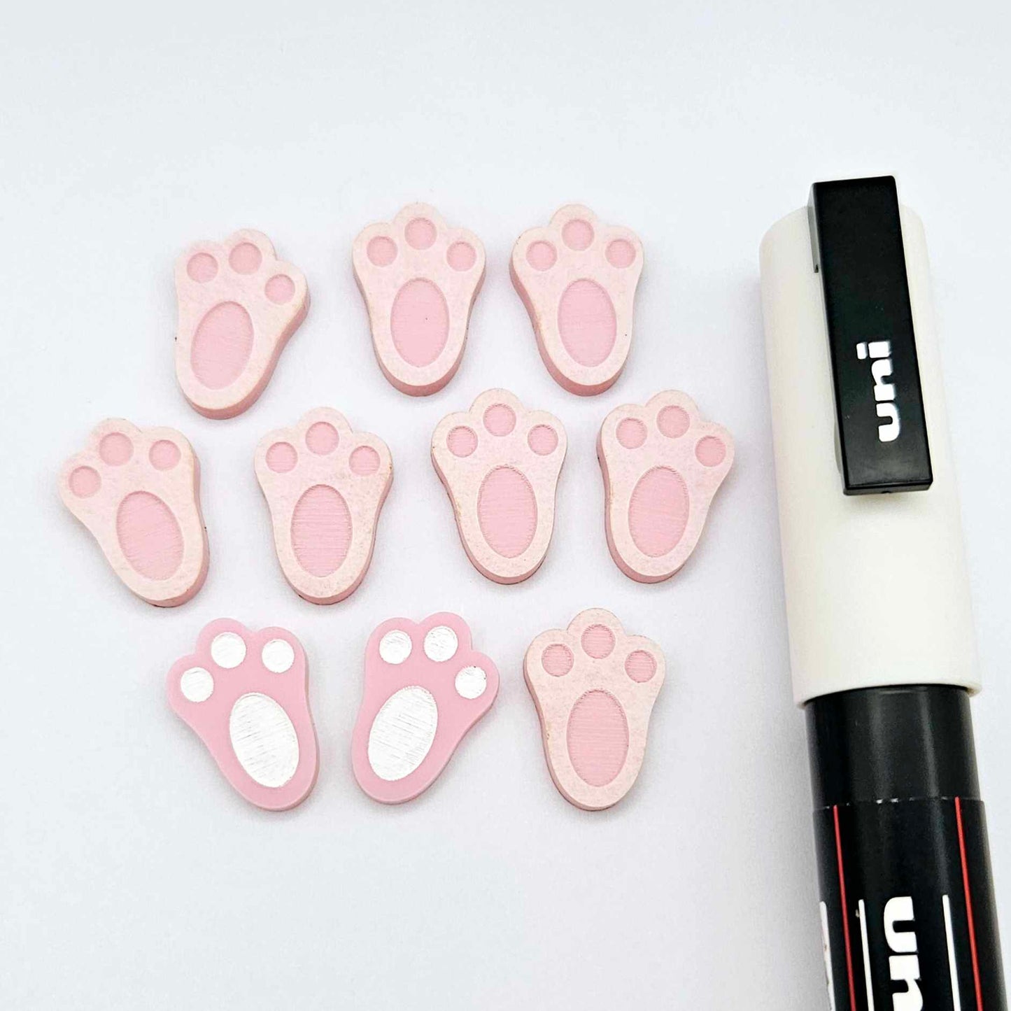 Pastel pink bunny paw print stud blanks showing two paint filled white and several unpainted pieces, with a white Posca paint pen included in the image