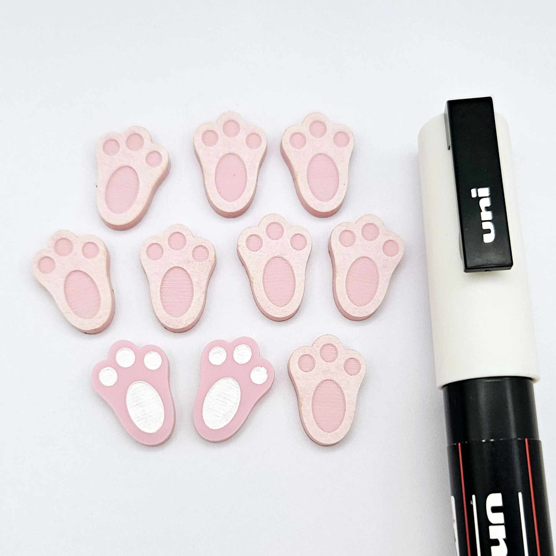 Pastel pink bunny paw print stud blanks showing two paint filled white and several unpainted pieces, with a white Posca paint pen included in the image