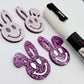 38mm purple glitter acrylic bunny dangle blanks with engraved smiley face, two paint filled white and two others unfilled with protective film on, shown with a White Posca paint pen