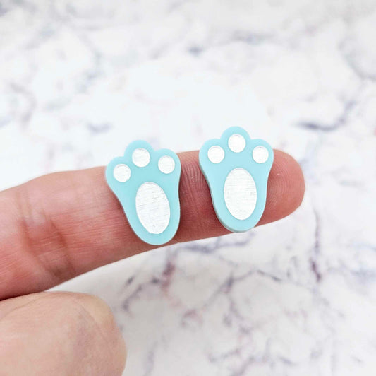 Close-up of two pastel aqua acrylic bunny paw print stud blanks with engraved pads paint filled white
