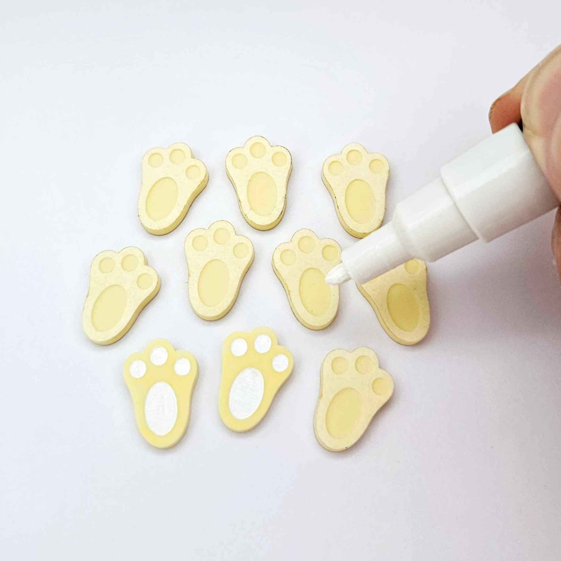 Pastel yellow bunny paw print stud blanks showing two paint filled white and several unpainted pieces, with a white Posca paint pen included in the image
