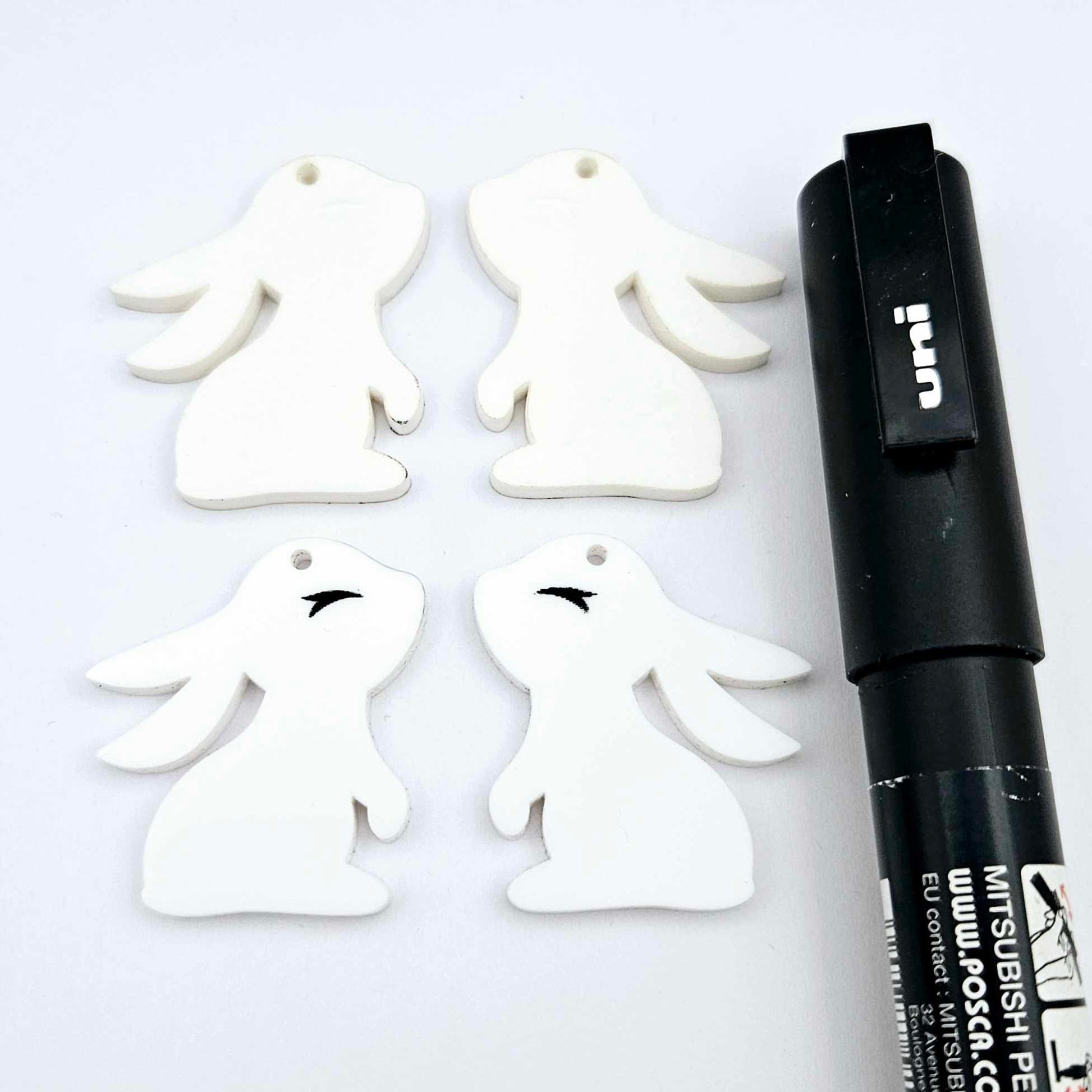 32mm white bunny dangle blanks showing paint filled black eyelashes on two pieces, with remaining pieces shown with protective paper as supplied