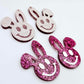 Hot pink glitter acrylic bunny dangle blanks with engraved smiley face, two paint filled white and two others unfilled with protective film on, shown with a White Posca paint pen