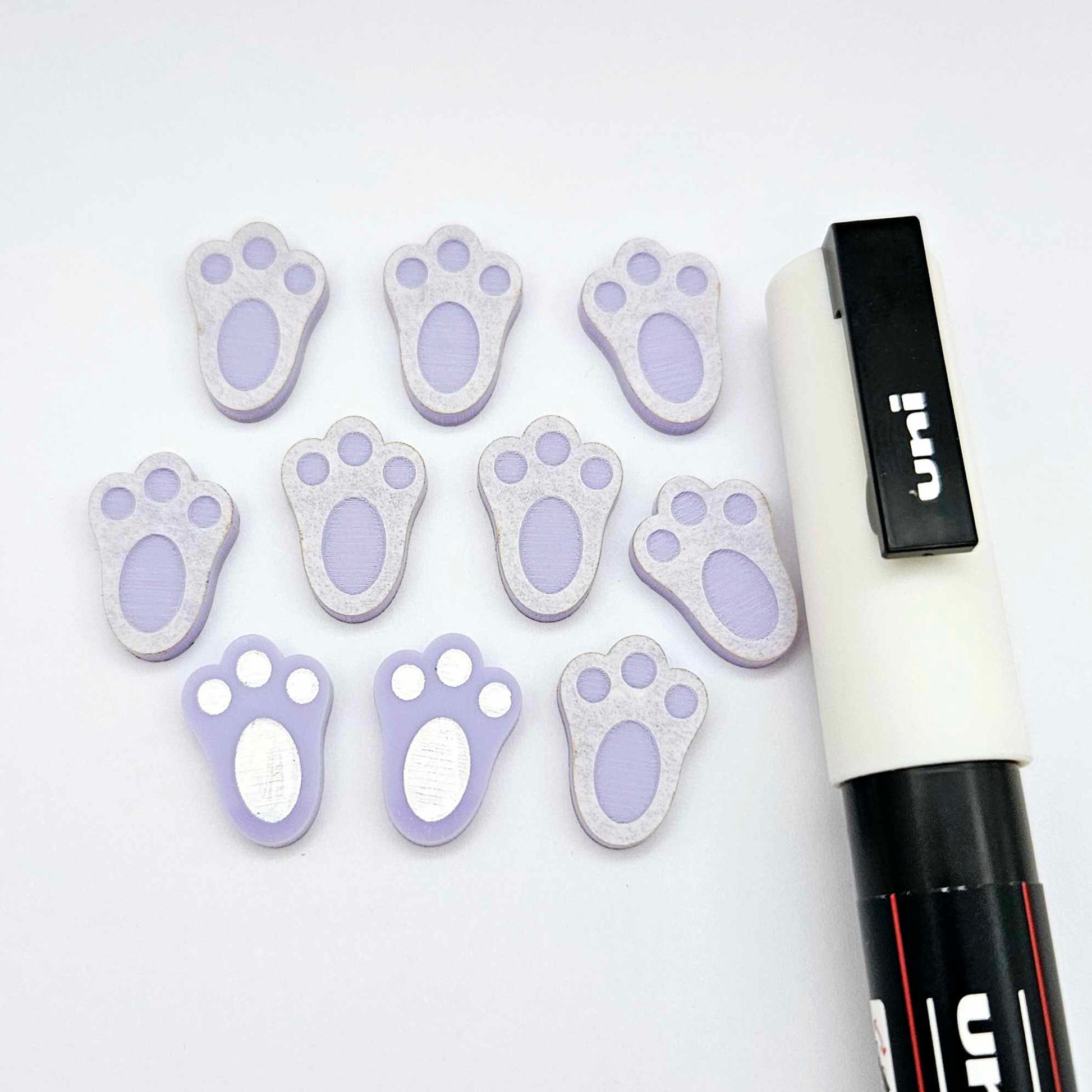 Pastel purple bunny paw print stud blanks showing two paint filled white and several unpainted pieces, with a white Posca paint pen included in the image
