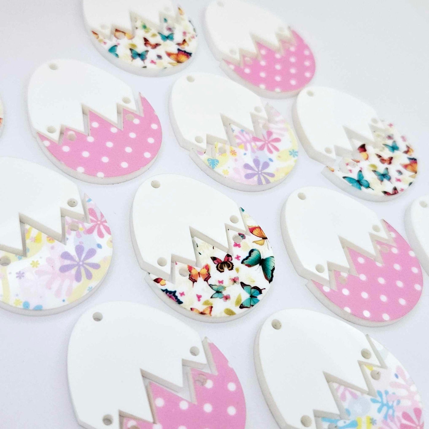 A mixture of cracked egg acrylic earring blanks unassembled, white top halves and different UV printed bottom halves