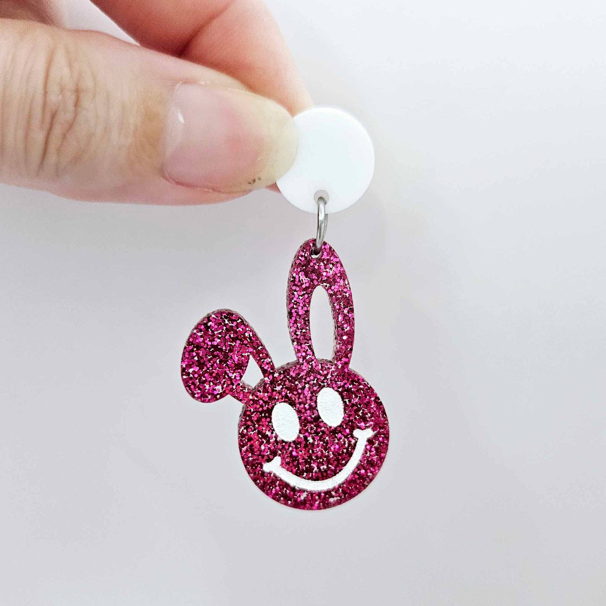 Hot pink glitter acrylic bunny dangle earring blank hanging from a 14mm white acrylic topper, bunny head with floppy ear and paint filled smiley face