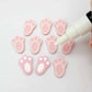 Pastel pink bunny paw print stud blanks showing two paint filled white and several unpainted pieces, with a white Posca paint pen included in the image