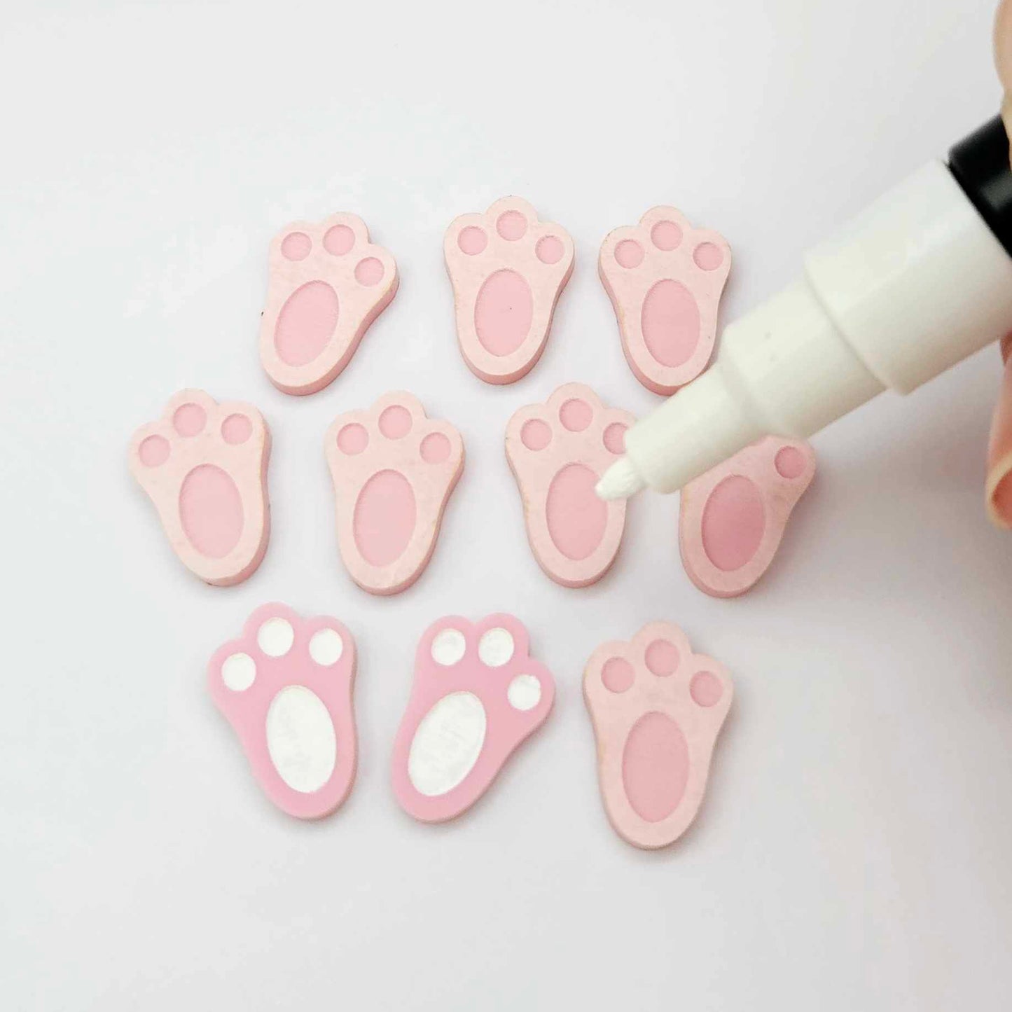 Pastel pink bunny paw print stud blanks showing two paint filled white and several unpainted pieces, with a white Posca paint pen included in the image