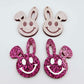 Hot pink glitter acrylic bunny dangle blanks with engraved smiley face, two paint filled white and two others unfilled with protective film on, shown with a White Posca paint pen