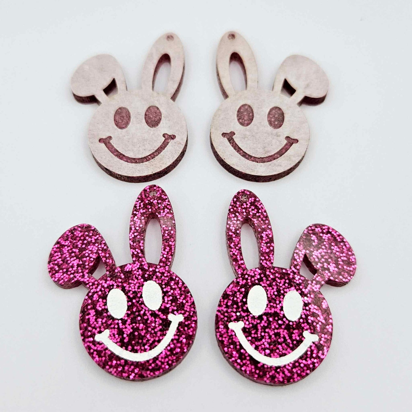 Hot pink glitter acrylic bunny dangle blanks with engraved smiley face, two paint filled white and two others unfilled with protective film on, shown with a White Posca paint pen