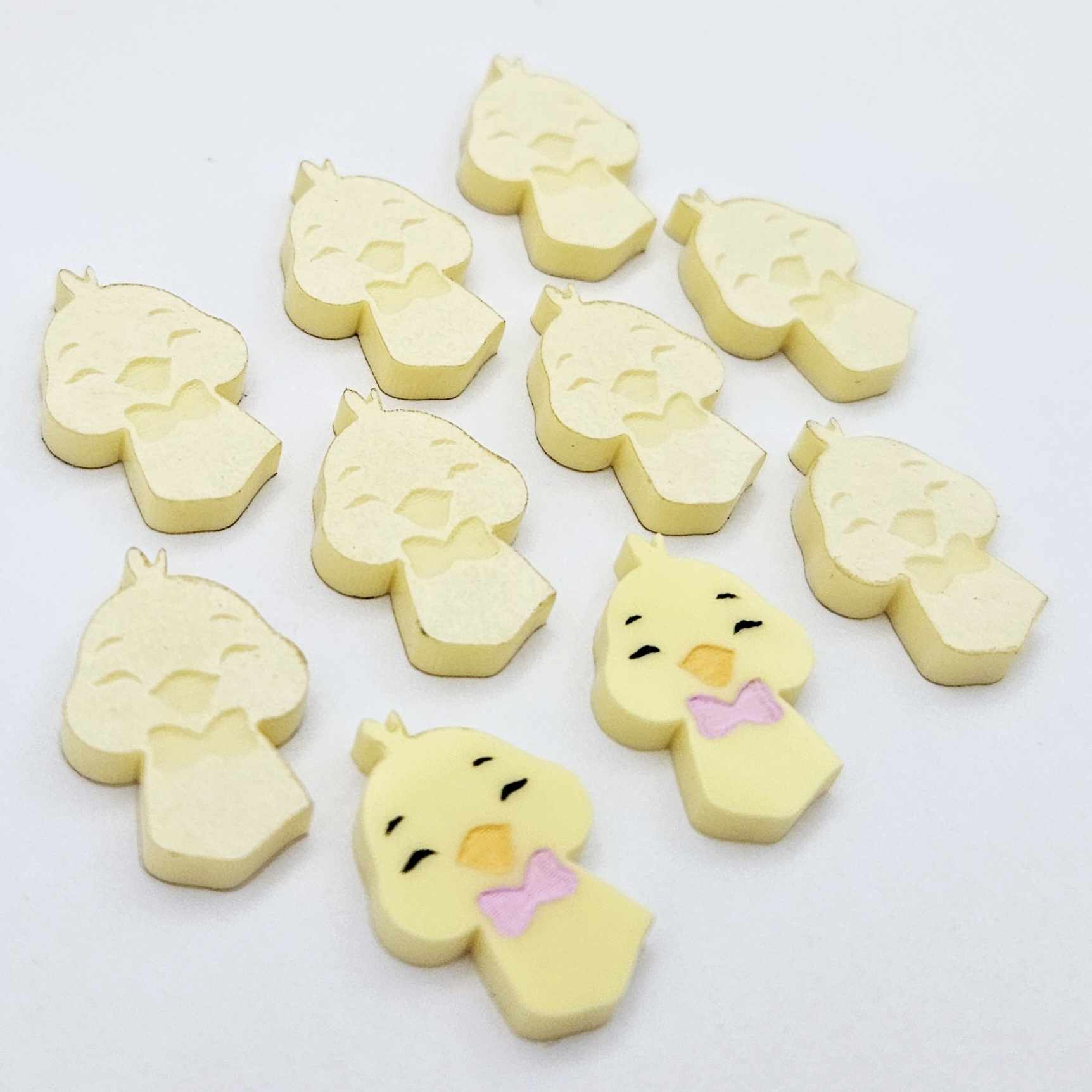 Pastel yellow acrylic chicken head stud blanks showing two paint filled examples and several unpainted pieces