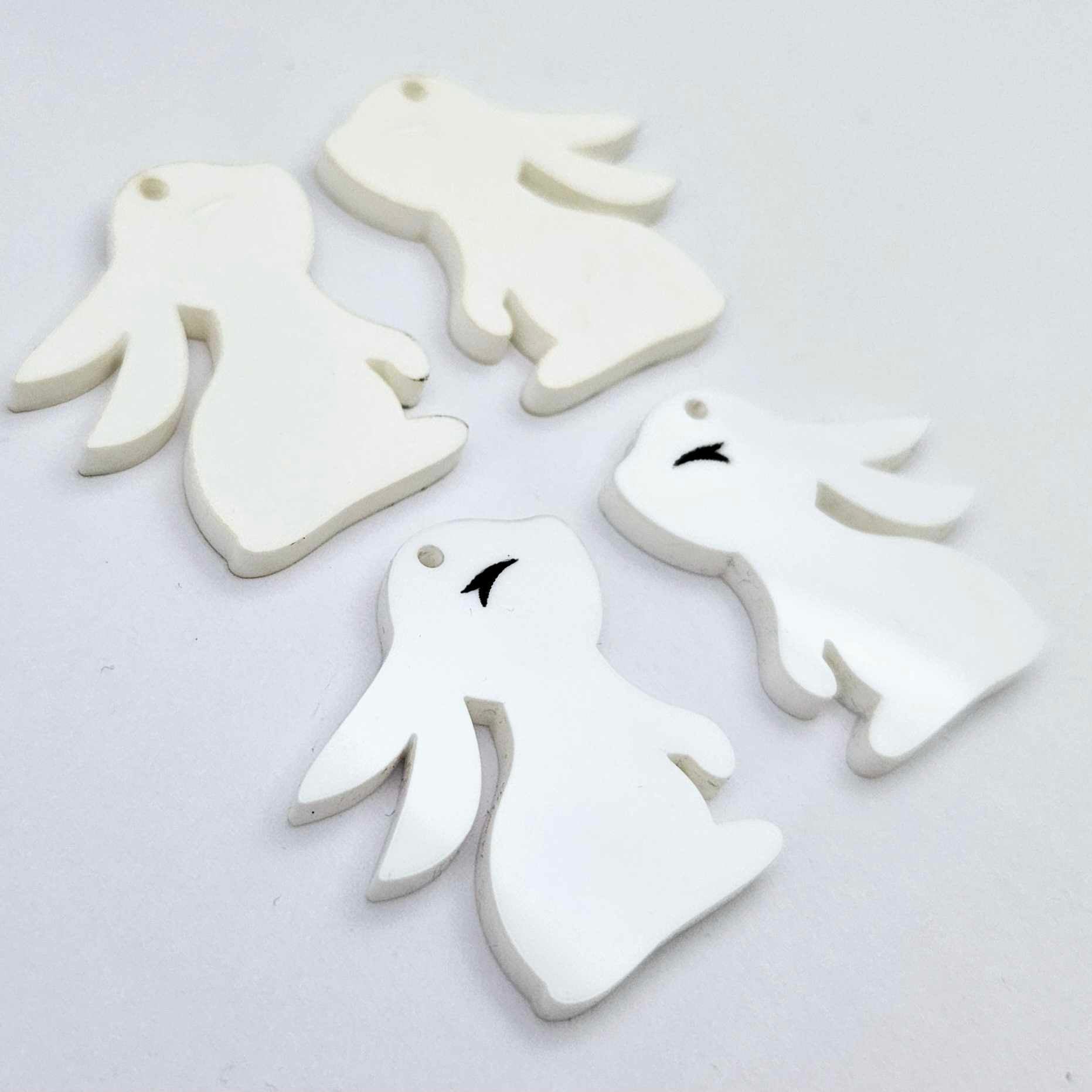 32mm white bunny dangle blanks showing paint filled black eyelashes on two pieces, with remaining pieces shown with protective paper as supplied