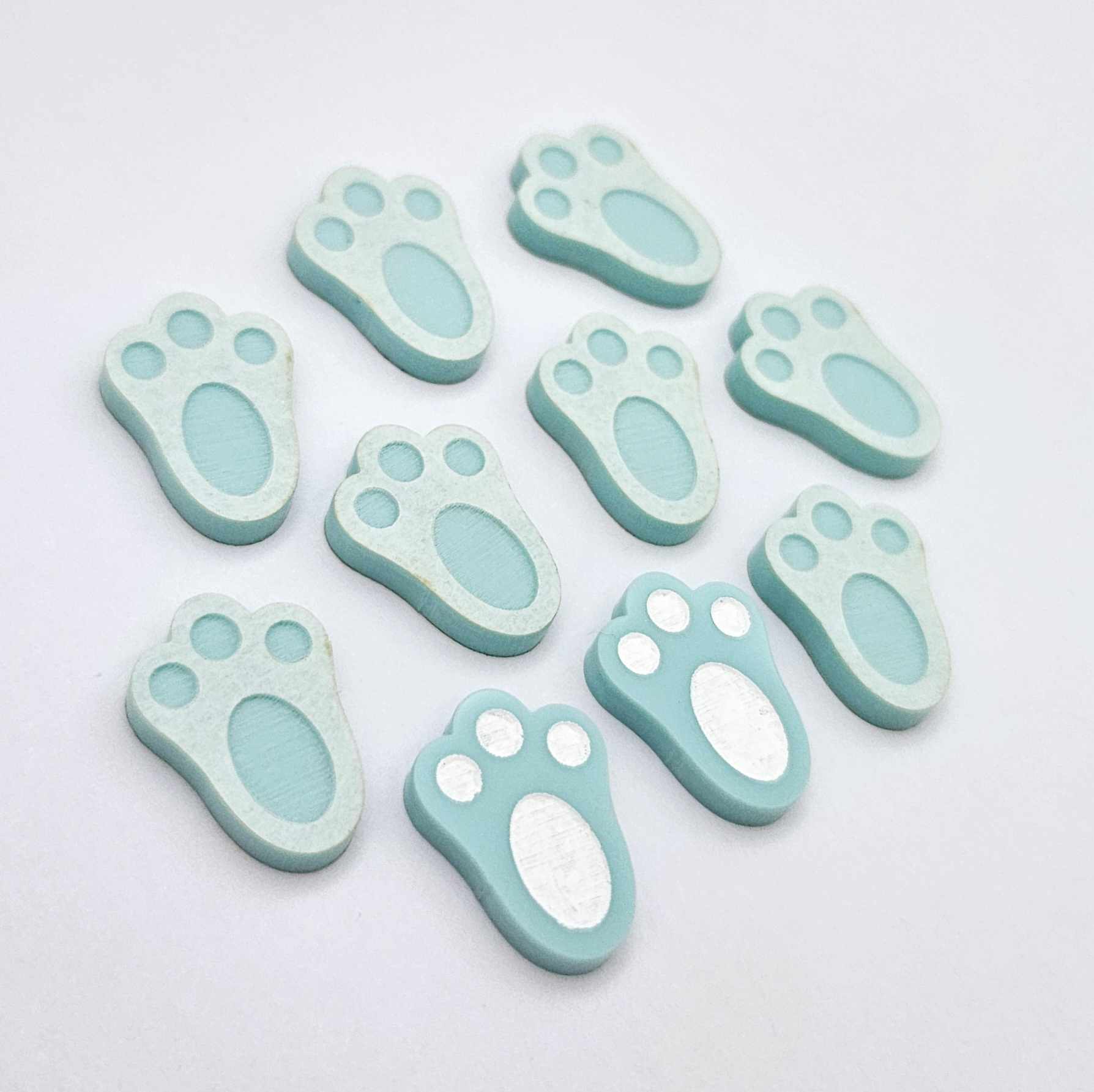Pastel aqua bunny paw print stud blanks showing two paint filled white and several unpainted pieces