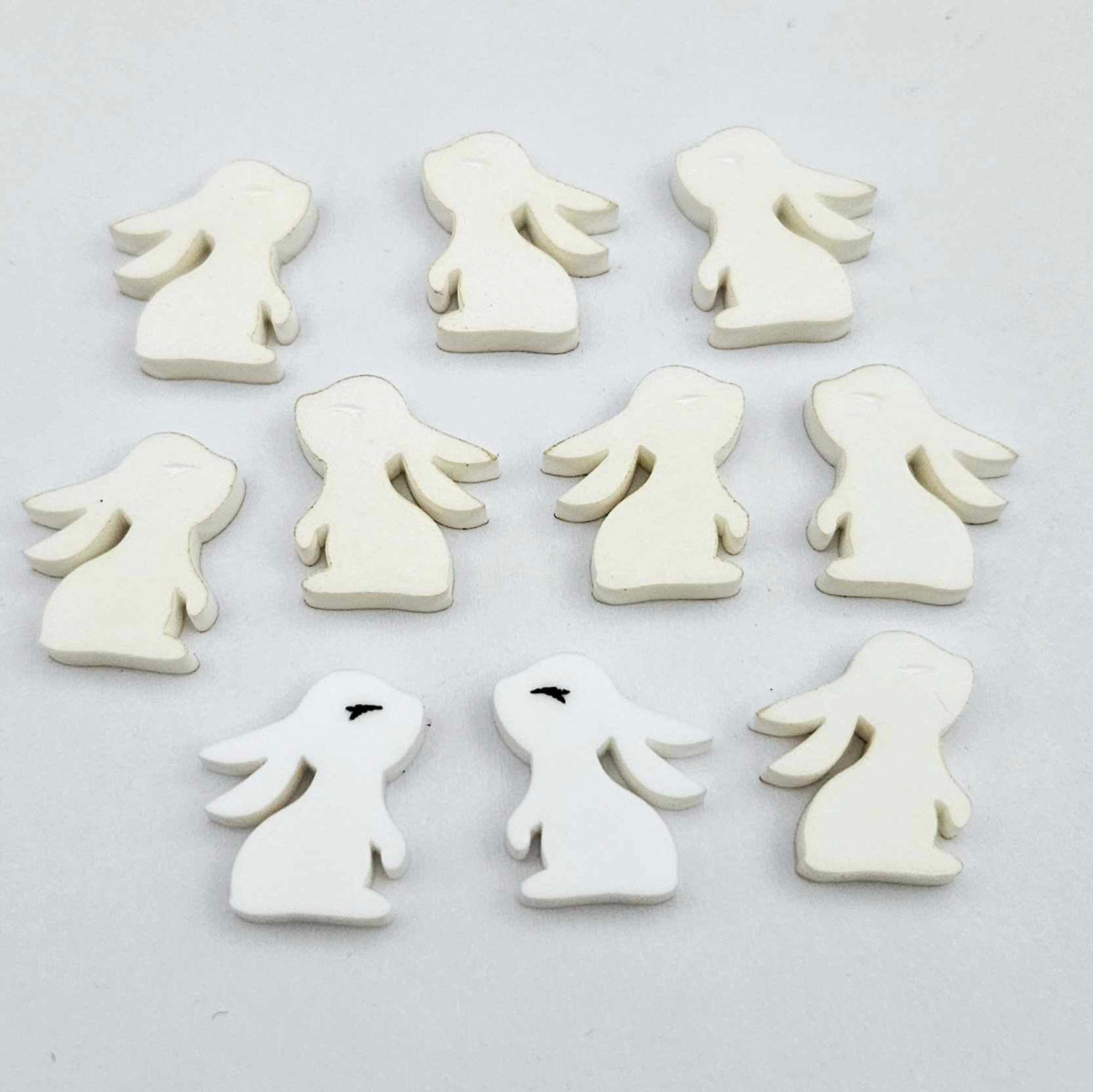 white acrylic bunny stud blanks showing finished paint filled black eyelashes on two studs, with the rest shown as supplied with protective film