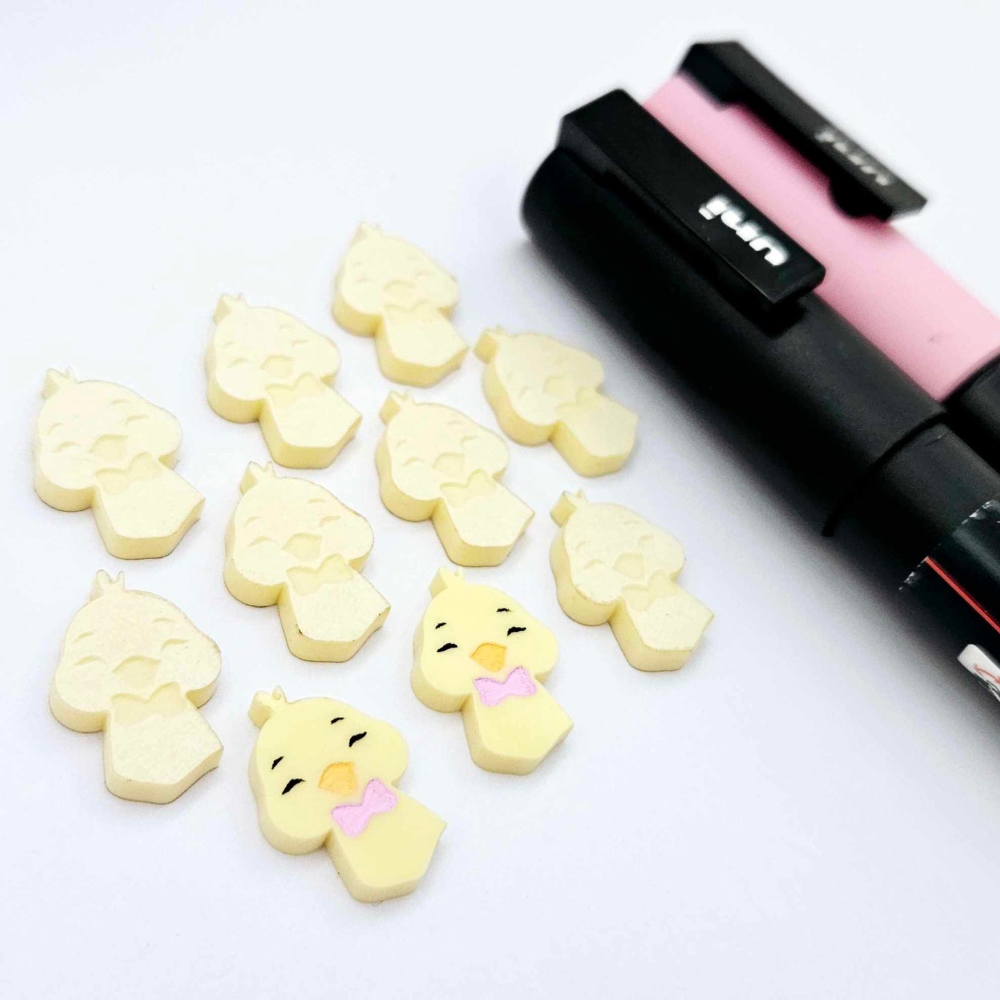 Pastel yellow acrylic chicken head stud blanks showing two paint filled examples and several unpainted pieces, with Posca paint pens included in the image