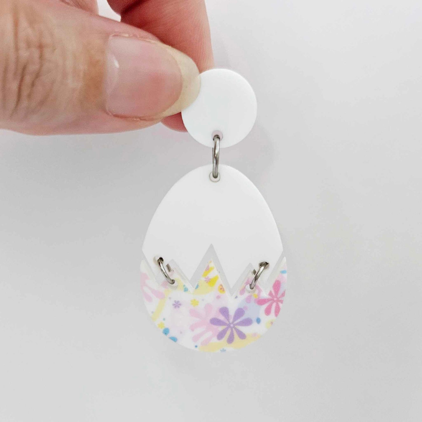 Assembled cracked egg acrylic dangle earring blank with white top and pastel pop UV printed bottom, hanging from a 14mm white earring topper