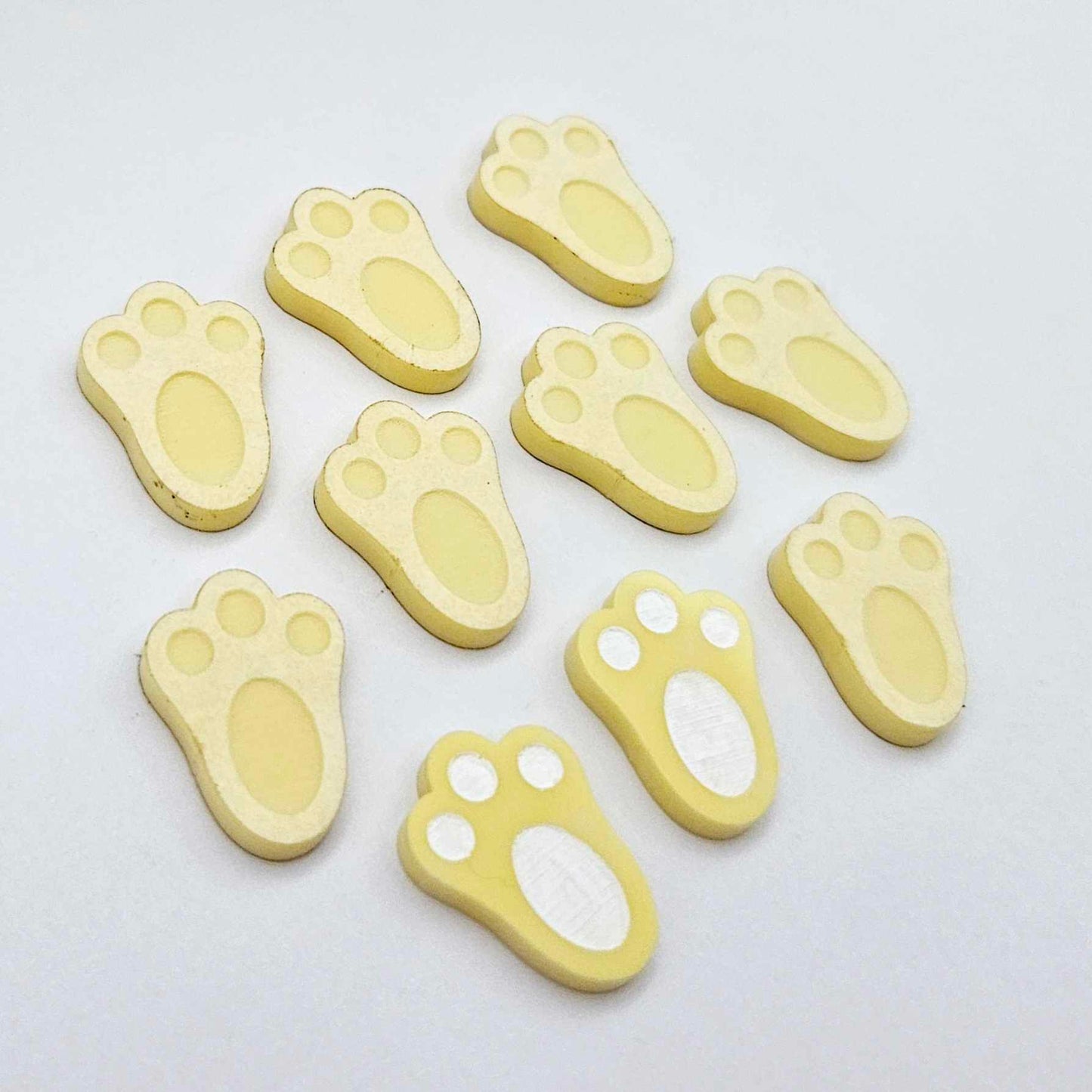 Pastel yellow bunny paw print stud blanks showing two paint filled white and several unpainted pieces