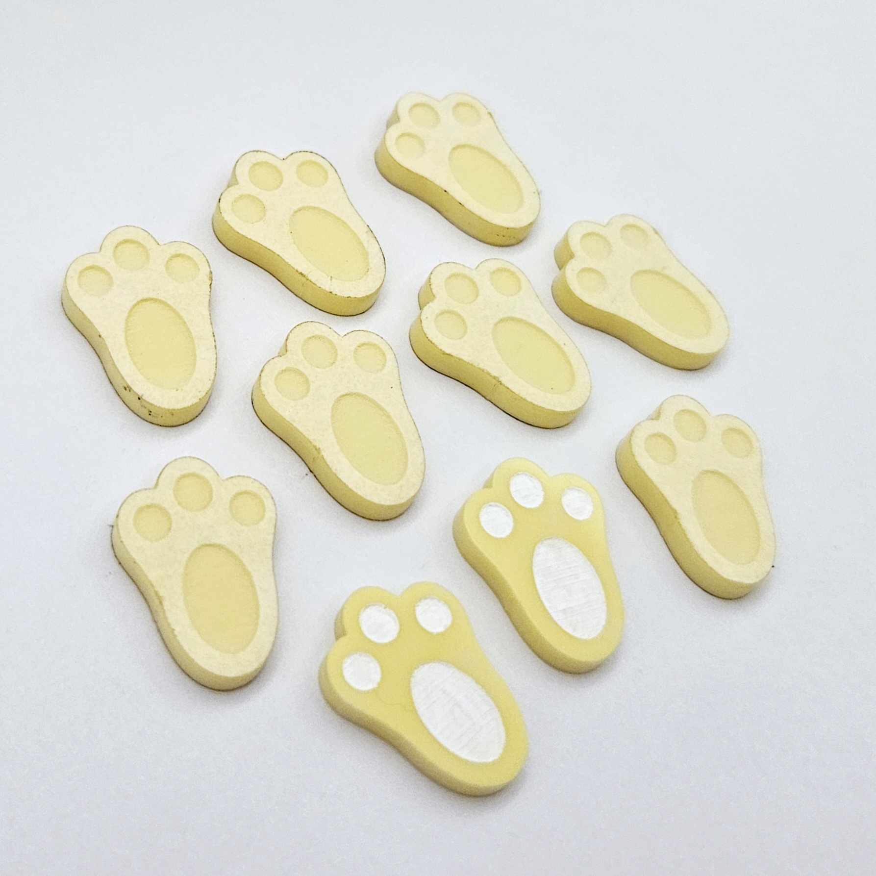 Pastel yellow bunny paw print stud blanks showing two paint filled white and several unpainted pieces