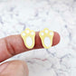 Close-up of two pastel yellow acrylic bunny paw print stud blanks with engraved pads paint filled white