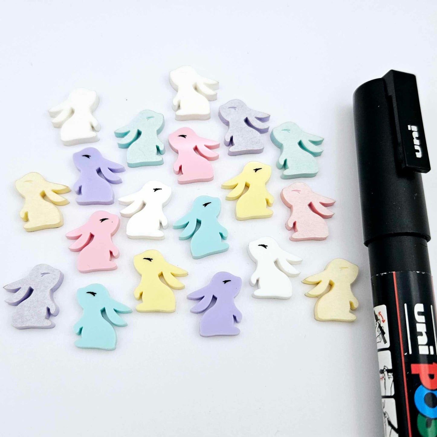 Pastel yellow, pink, purple, aqua and white bunny stud blanks (mixed pack) showing finished paint filled black eyelashes on two studs, with the rest shown as supplied with protective film