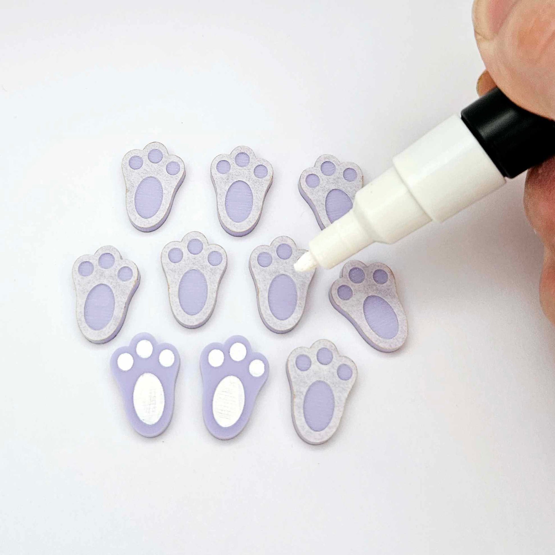 Pastel purple bunny paw print stud blanks showing two paint filled white and several unpainted pieces, with a white Posca paint pen included in the image