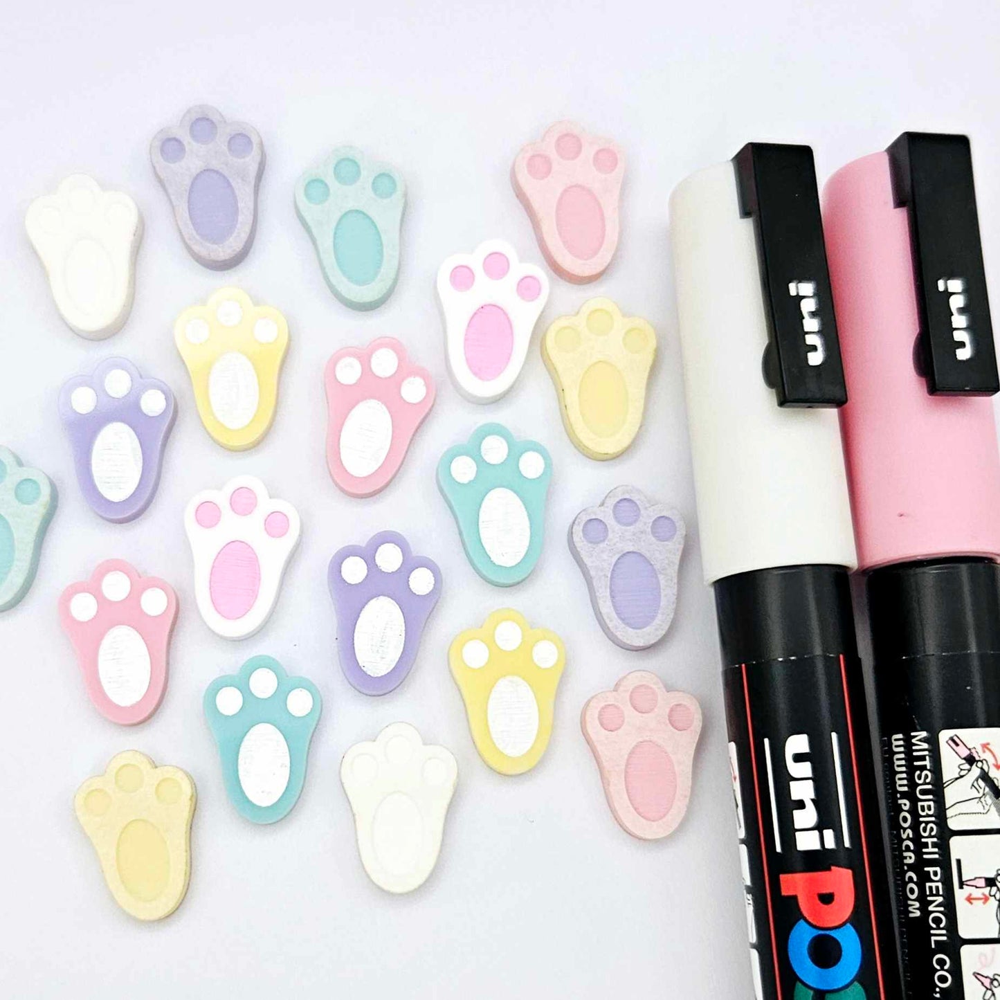white and pastel bunny paw print stud blanks showing some paint filled and several unpainted pieces, with a Light Pink and White Posca paint pen included in the image
