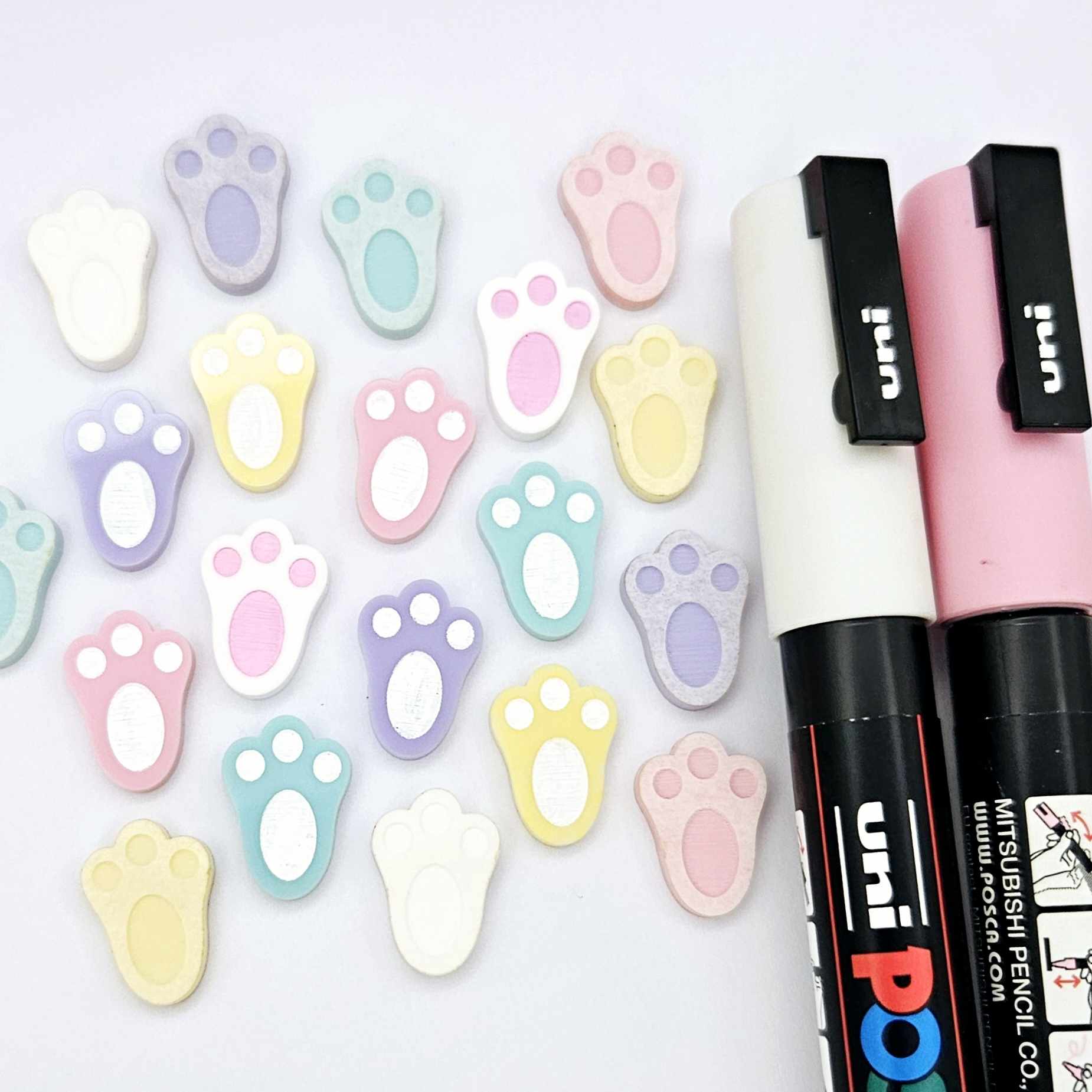 white and pastel bunny paw print stud blanks showing some paint filled and several unpainted pieces, with a Light Pink and White Posca paint pen included in the image