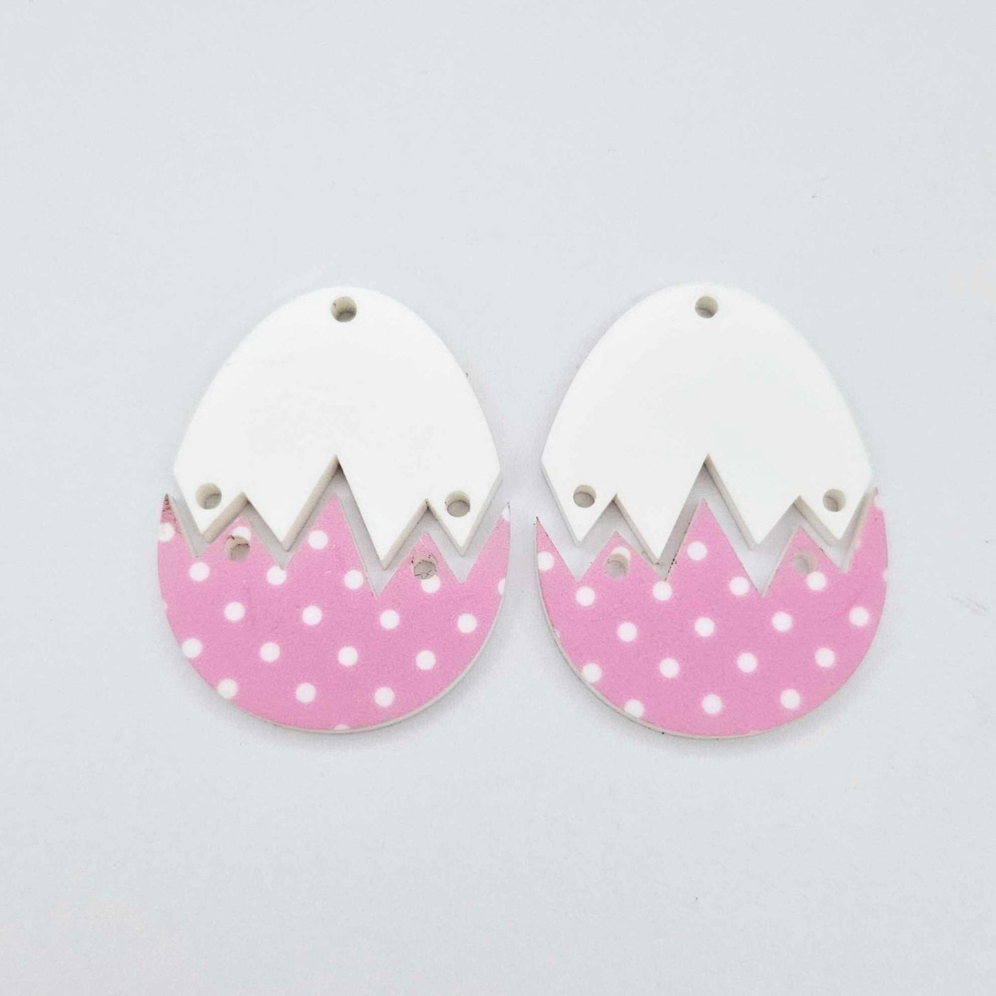 Two cracked egg earring blanks unassembled, white top halves and pastel pink polka dot UV printed bottom halves