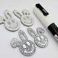 38mm silver glitter acrylic bunny dangle blanks with engraved smiley face, two paint filled white and two others unfilled with protective film on, shown with a White Posca paint pen