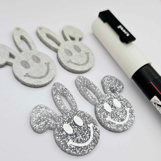 38mm silver glitter acrylic bunny dangle blanks with engraved smiley face, two paint filled white and two others unfilled with protective film on, shown with a White Posca paint pen